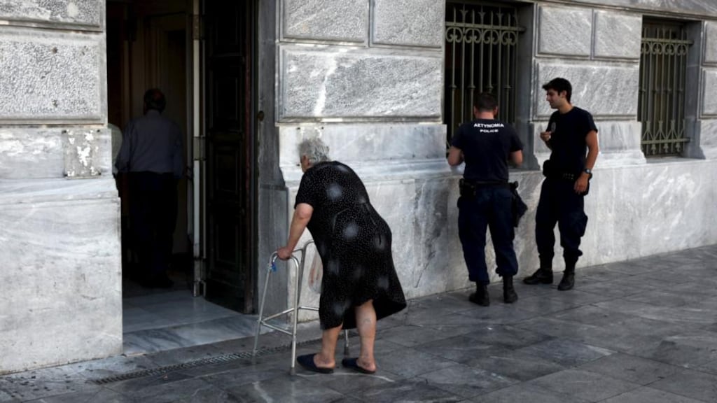 Pensioner arrives to receive part of her pension as police officers stand by at a National Bank branch in Athens, Photograph: Reuters/Yiannis Kourtoglou