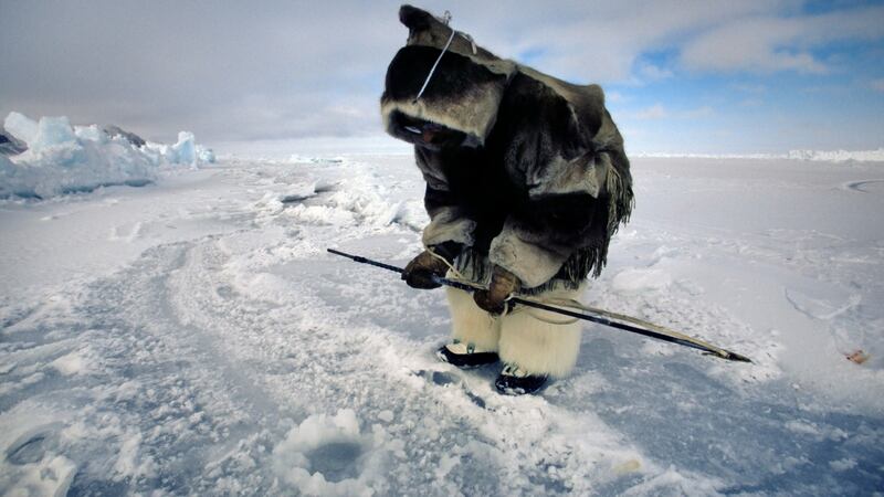 An Inuit man stands holding harpoon over seal hole, waiting for a seal to return. Photograph: Getty Images