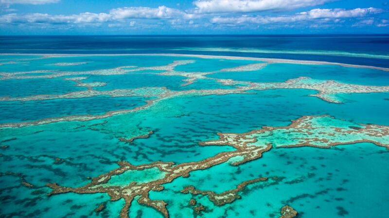 Aerial photo of Great barrier reef showing reef area with some blue water and slightly cloudy sky in background.