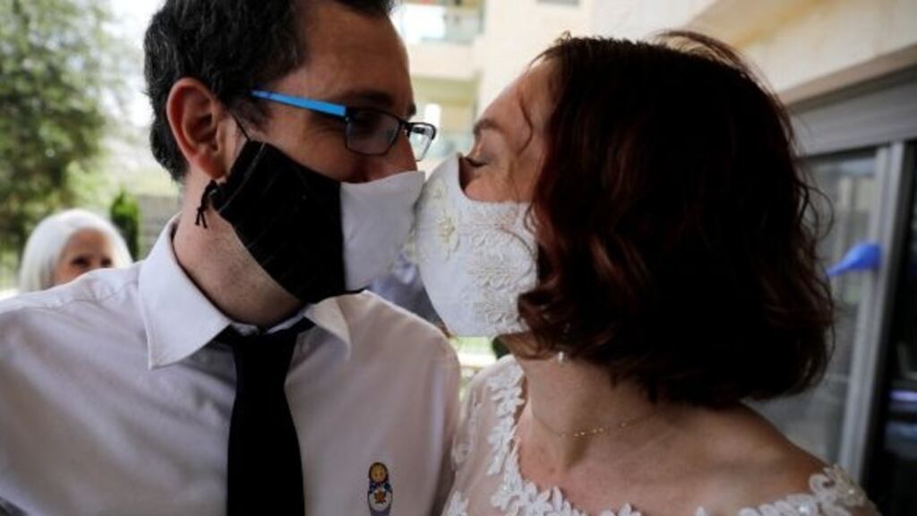 Bride, Osnat Baron, and groom, Yaniv Jenger, kiss while wearing face masks during their wedding party in Jerusalem. Photograph: Ronen Zvulun/Reuters