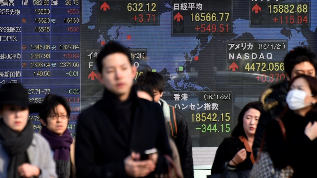 Pedestrians walk past a share prices board showing the numbers from various world stock markets in Tokyo