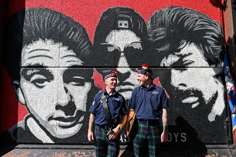 Members of a flute band chat in front of a mural of the band The Beastie Boys as they prepare to take part in a Twelfth of July parade in Belfast. Photograph: Charles McQuillan/Getty
