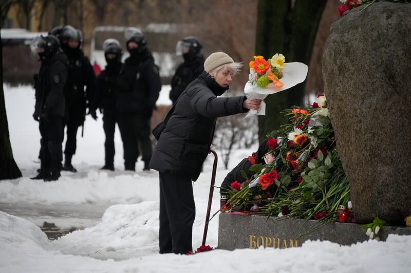 Police officers stand guard as a woman lays flowers at a makeshift memorial to Alexei Navalny in St Petersburg (Dmitri Lovetsky/AP)