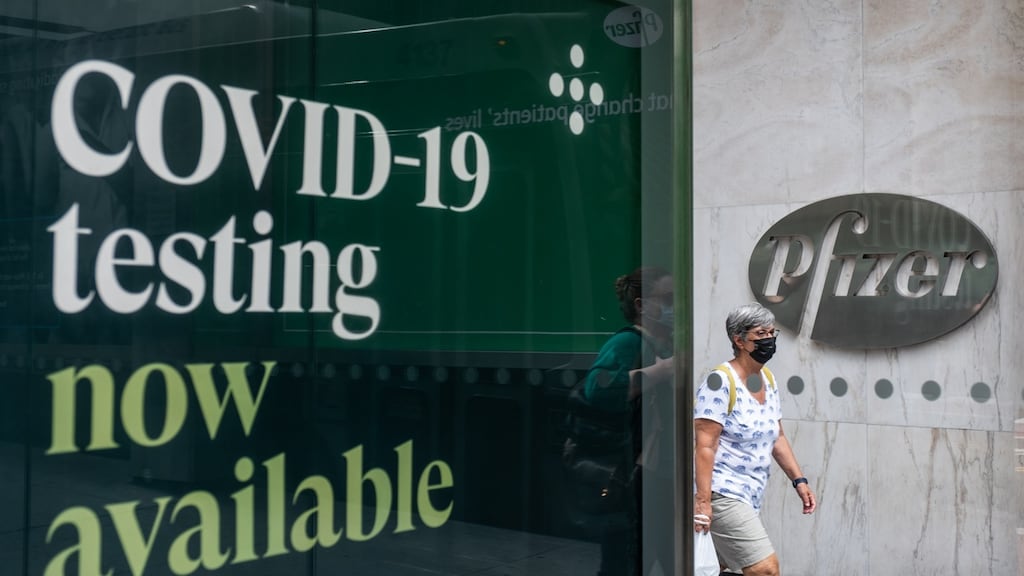 A pedestrian wearing a protective mask passing in front of a sign outside Pfizer headquarters in New York.