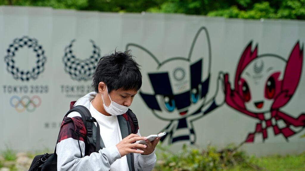 A young man wearing a face mask walks past Tokyo Olympics logos in Tokyo. Photo: Franck Robichon/EPA