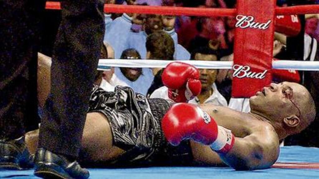 A dazed and bloodied Mike Tyson at the feet of referee Eddie Cotton after being floored by Lennon Lewis in the eighth round of their WBC/IBF heavyweight championship bout in Memphis, Tennessee