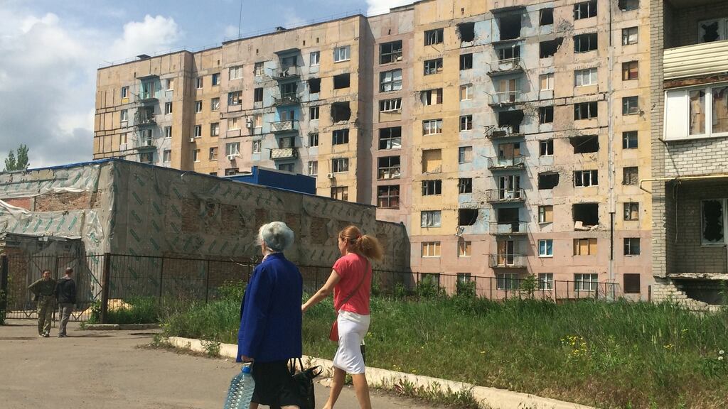 Two women walk past an apartment block damaged by shelling in Avdiivka, eastern Ukraine: many of the apartment building’s windows have been shattered during two years of sporadic shelling. Photograph: Daniel McLaughlin