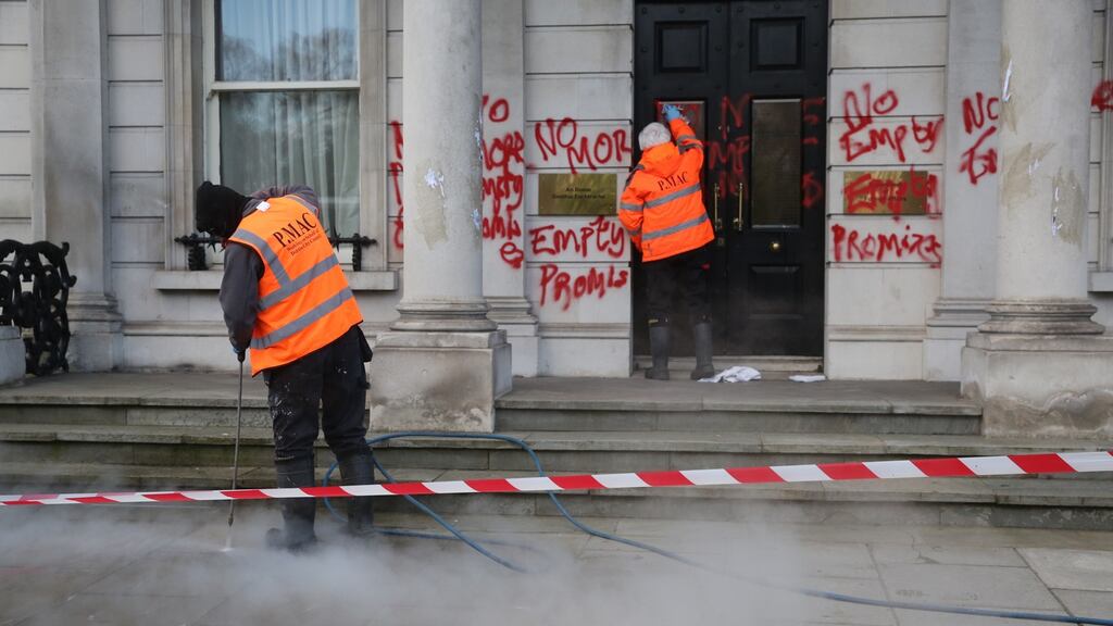 Cleaners are seen on Friday removing graffiti from the entrance to Iveagh House in Dublin. Two people have been charged in connection with the incident. Photograph: Collins