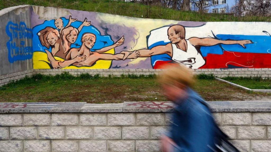 A woman passes a graffiti artwork depicting Russian president Vladimir Putin extending a hand to the Ukrainian people in the Crimean city of Simferopol yesterday. Photograph: Shamil Zhumatov/Reuters