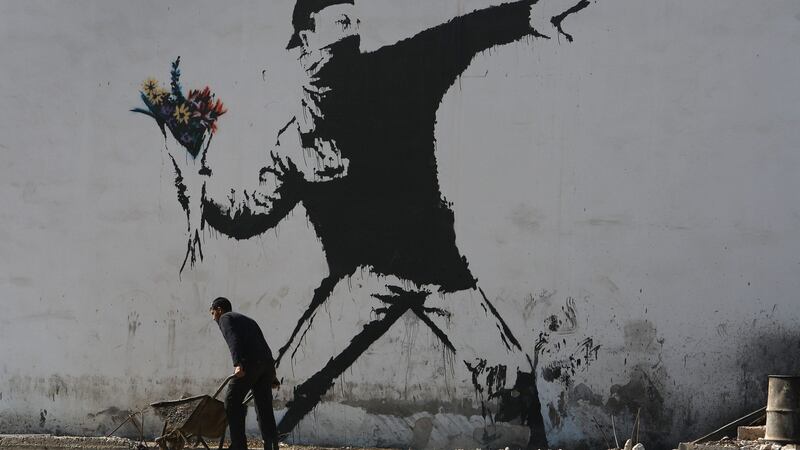 A Palestinian labourer works under a large wall painting by graffiti artist Banksy in Bethlehem. Photograph: David Silverman/Getty Images