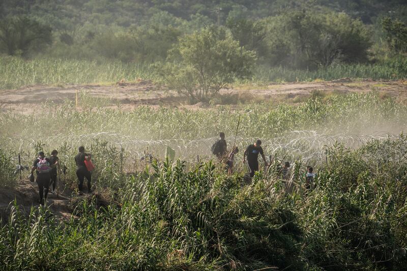 Asylum-seeking migrants search for an opening in a barrier of concertina wire along the Rio Grande river. Photograph: Go Nakamura/New York Times