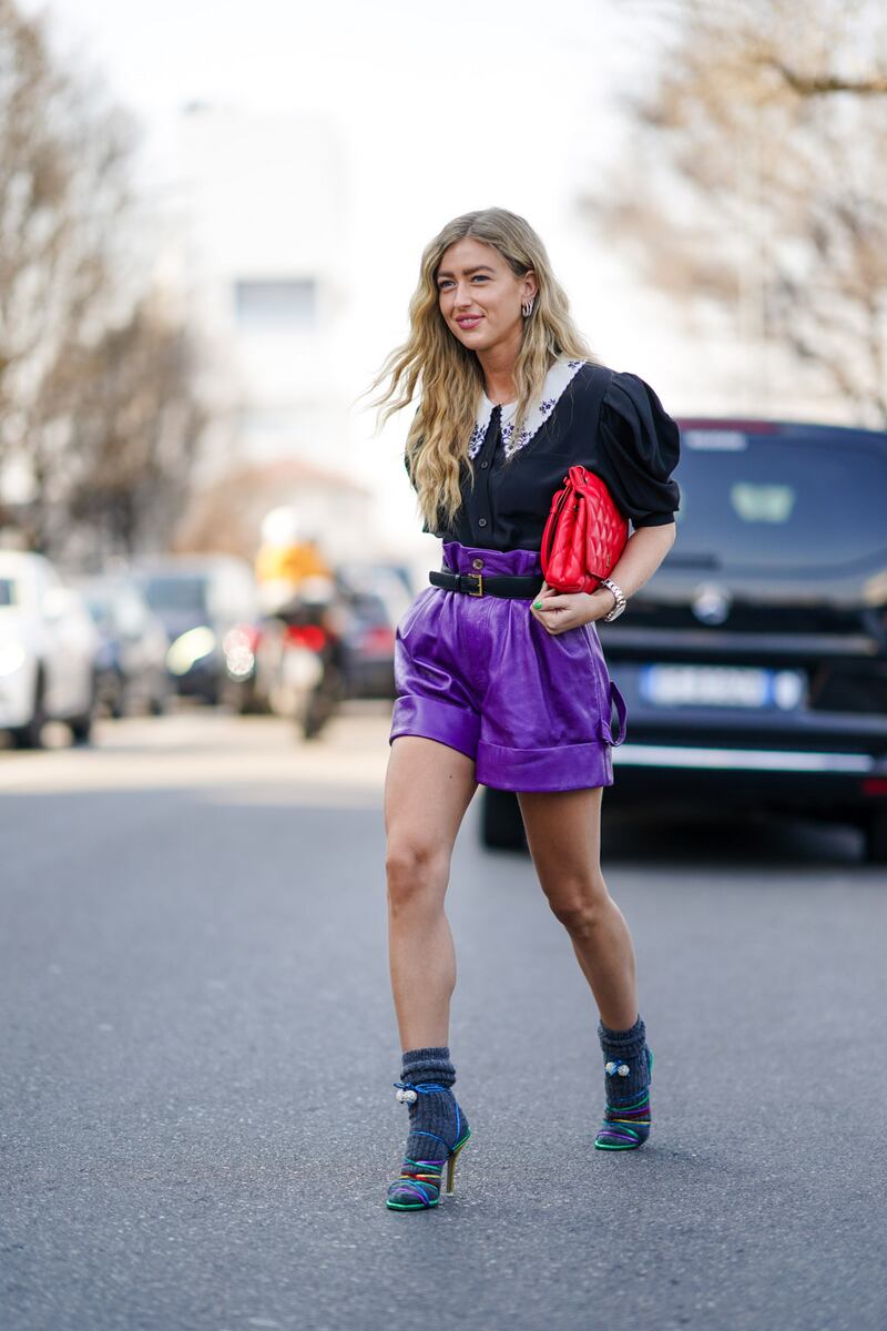 Emili Sindlev wears a ruffled black shirt with puff shoulder pads, a red quilted bag, purple leather shorts, gray wool socks, multicolor shoes, outside MSGM, during Milan Fashion Week Fall/Winter 2020-2021. Photograph: Edward Berthelot/Getty