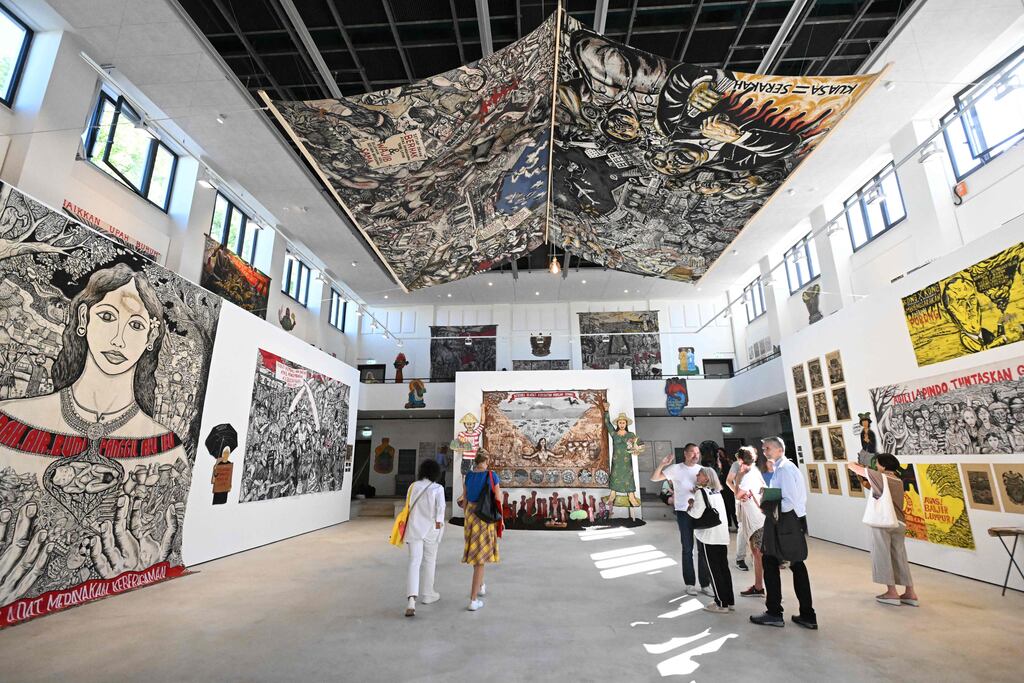 Visitors stand among works of the collective Taring Padi from Indonesia, at the Hallenbad Ost, one of the venues of the documenta fifteen contemporary art exhibition, in Kassel, central Germany, on June 16, 2022. - documenta 15 tales place in Kassel from June 18 to September 25, 2022 and is curated by the Indonesian artists' collective ruangrupa. - RESTRICTED TO EDITORIAL USE - MANDATORY MENTION OF THE ARTIST UPON PUBLICATION - TO ILLUSTRATE THE EVENT AS SPECIFIED IN THE CAPTION (Photo by Ina FASSBENDER / AFP) / RESTRICTED TO EDITORIAL USE - MANDATORY MENTION OF THE ARTIST UPON PUBLICATION - TO ILLUSTRATE THE EVENT AS SPECIFIED IN THE CAPTION / RESTRICTED TO EDITORIAL USE - MANDATORY MENTION OF THE ARTIST UPON PUBLICATION - TO ILLUSTRATE THE EVENT AS SPECIFIED IN THE CAPTION (Photo by INA FASSBENDER/AFP via Getty Images)