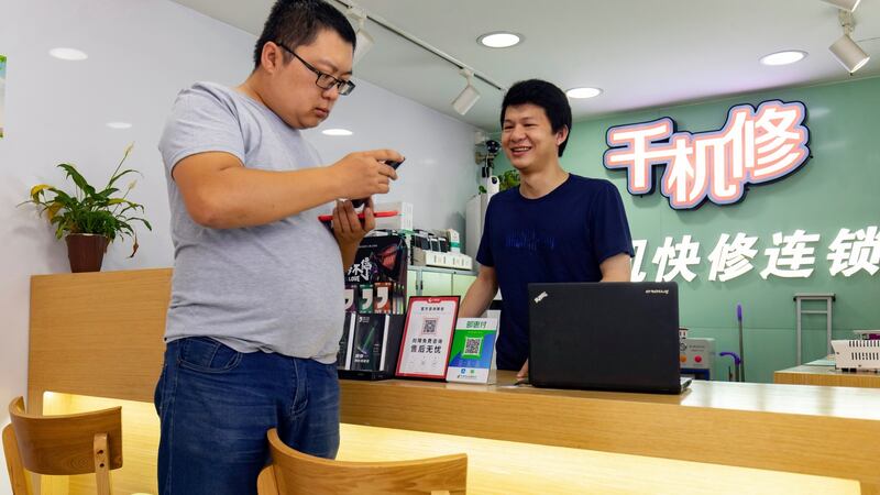 Huang Yulong assists a customer at the shop where he works repairing mobile phones in Guangzhou. Photograph: Qilai Shen/The New York Times
