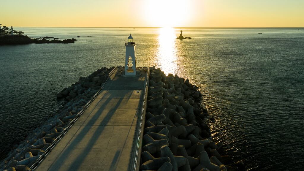 Pier with the sun setting behind a distant lighthouse in the Sea of Japan/East Sea. Photograph: Fábio Nascimento