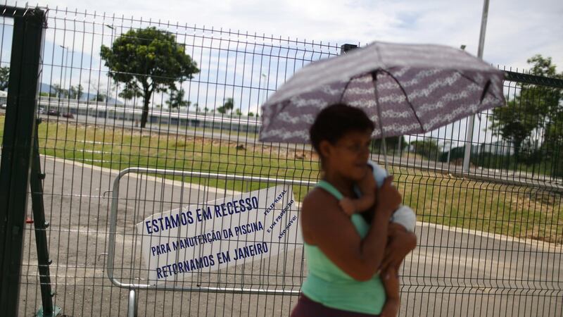 A woman carries a baby in front of the Deodoro Sports Complex, which was used for the Rio 2016 Olympic Games, in Rio de Janeiro, Brazil, February 7th, 2017. The clapboard reads: “ We are in recess for maintenance of the pool, we will return in January. Merry Christmas and Happy new year”. Photo: Pilar Olivares/Reuters