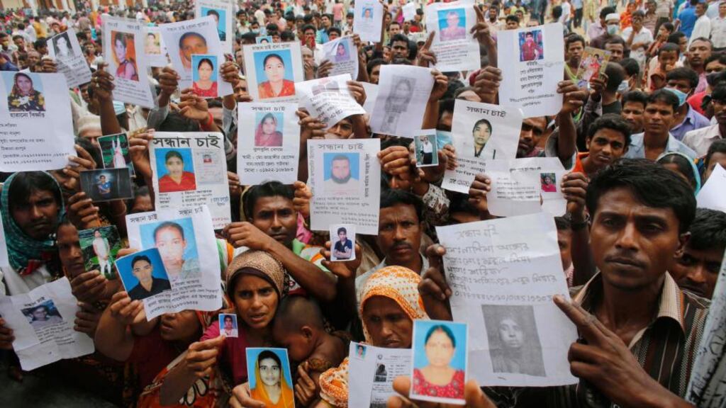 Relatives show pictures of garment workers believed to be trapped under the rubble of the collapsed Rana Plaza building last year. Clothes brands have been criticised for not doing enough to help families of victims. Photograph: Reuters