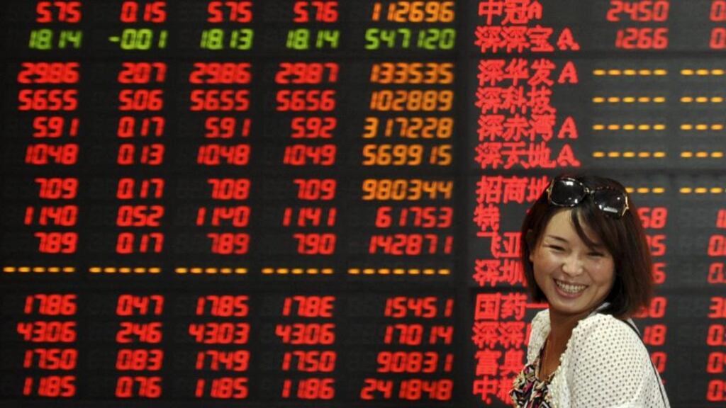An investor smiles as she walks past an electronic board showing stock information at a brokerage house in Fuyang, China, yesterday. Photograph: Reuters