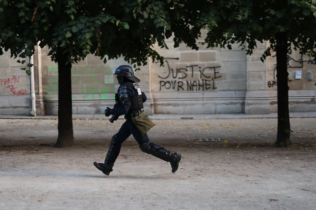 A riot police officer runs past a graffiti reading 'Justice for Nahel' in the Tuileries garden in Paris. Photograph: Charly Triballeau/AFP via Getty