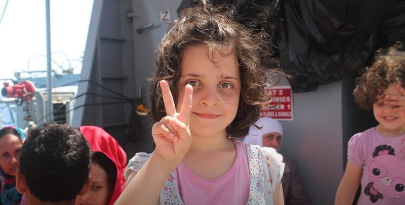 A migrant child gives a peace sign after she is brought on board the ‘LE Niamh’ on Wednesday during the rescue of more than 550 people from a barge off the coast of Libya. Photograph: Defence Forces