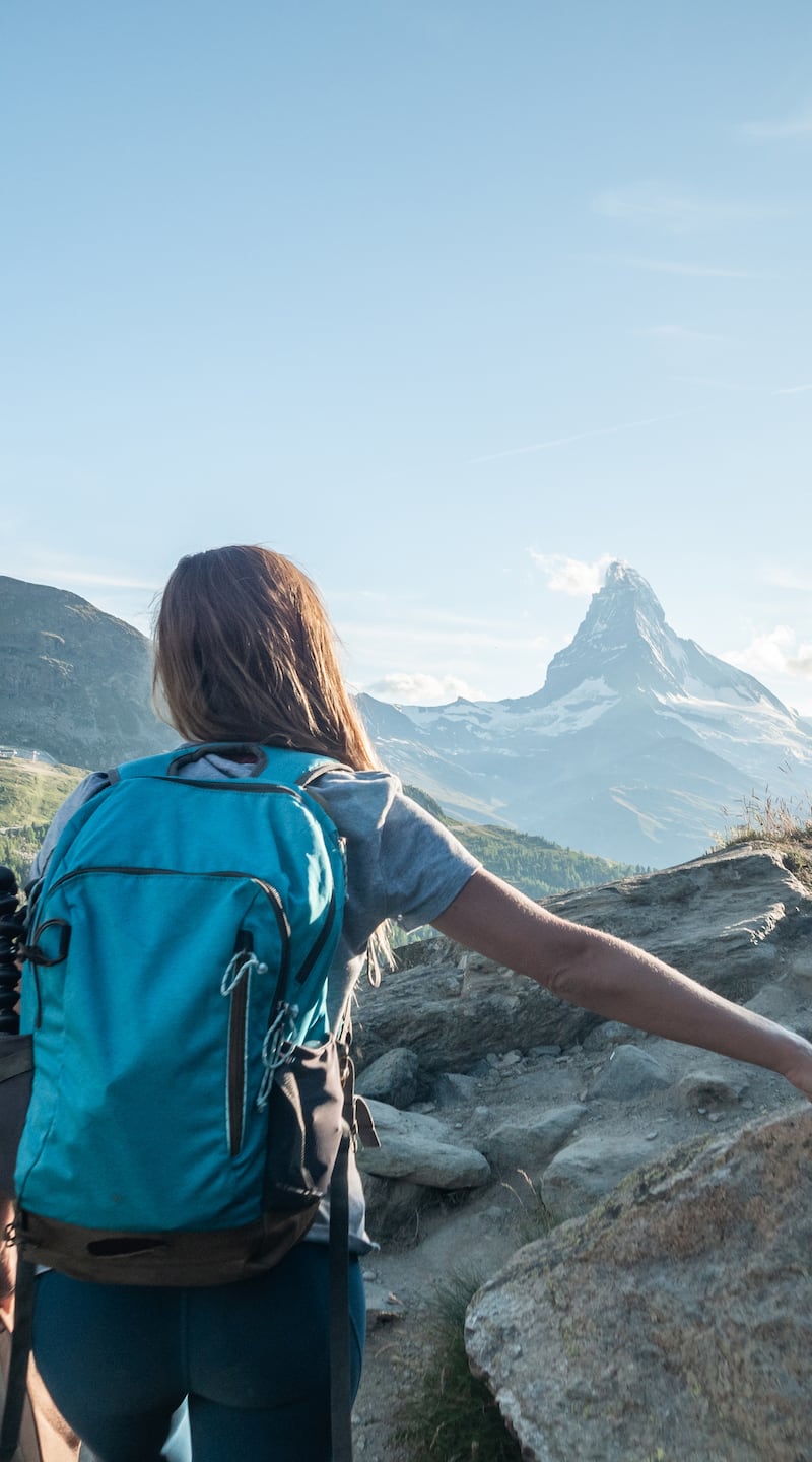 View of woman hiking on mountain trail looking at spectacular Matterhorn peak, Switzerland