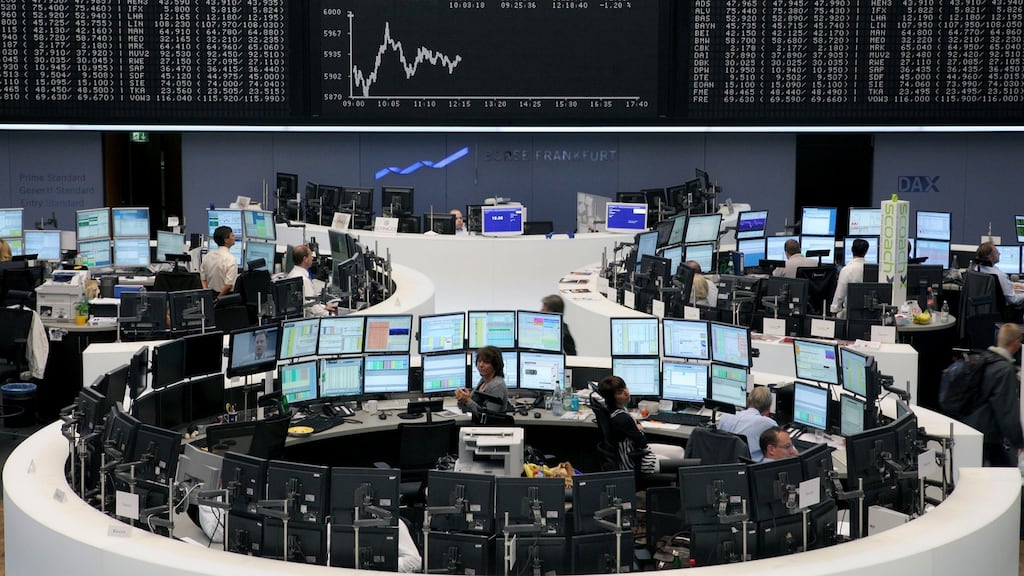 Financial traders work at their desks underneath a display of the DAX Index curve at the Frankfurt Stock Exchange in Germany