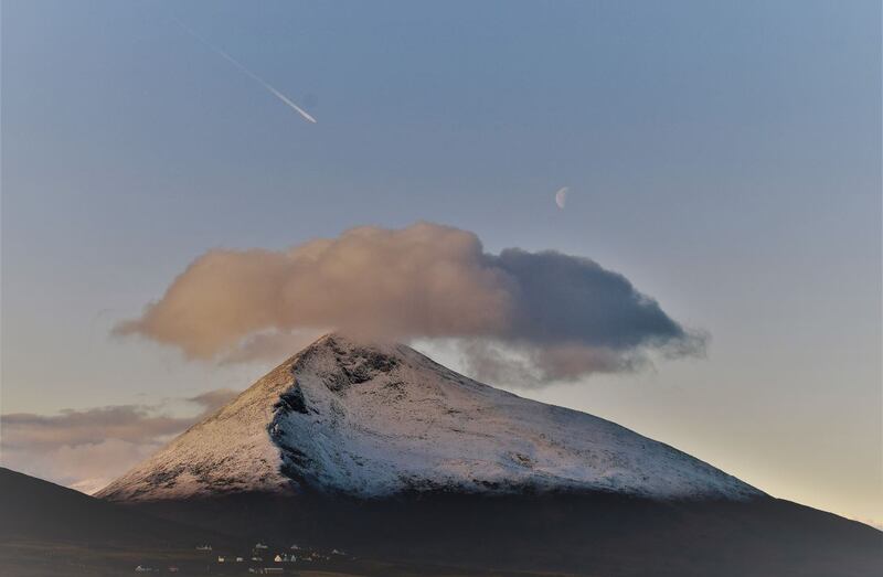 A snowy Sliabhmór mountain on Achill Island with a passing plane and a waning crescent moon. Photograph: Katrina Gallagher