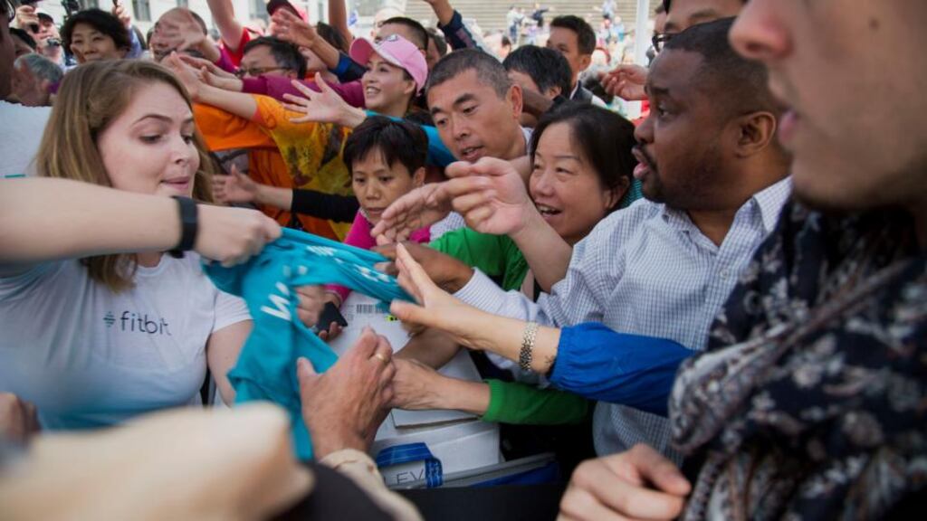People reach for free Fitbit Inc. shirts after the company’s initial public offering outside of the New York Stock Exchange. Photographer: Michael Nagle/Bloomberg