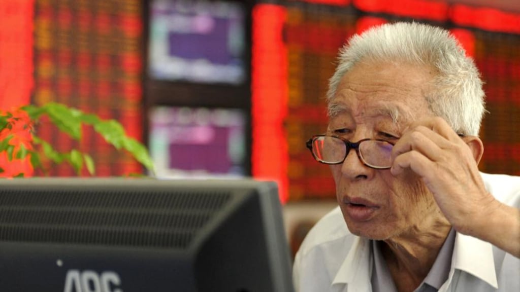 An investor adjusts his glasses as he looks at a computer screen in front of an electronic board showing stock information at a brokerage house in Fuyang, Anhui province, China. Photograph: China Daily/Reuters