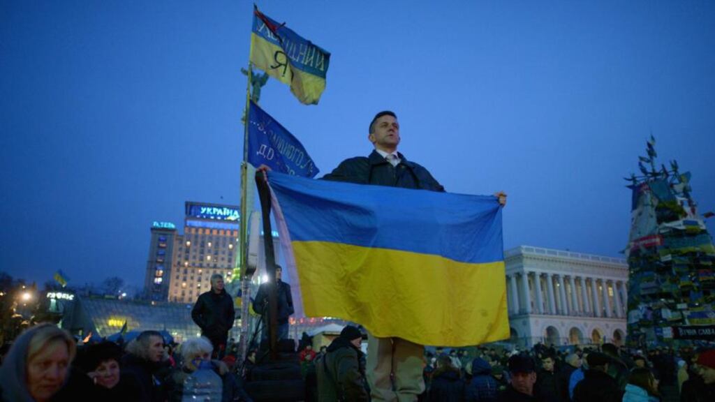 A man stands on a wall holding a Ukrainian flag while listening to speakers on stage in Independence Square today in Kiev. Photograph: Jeff J Mitchell/Getty Images