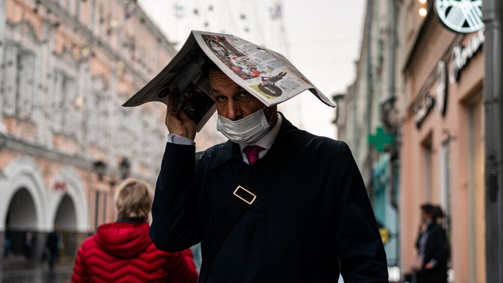 A man wearing a face mask uses a newspaper to protect himself from the rain in central Moscow on Thursday. Photograph:   Dimitar Dilkoff/AFP via Getty Images