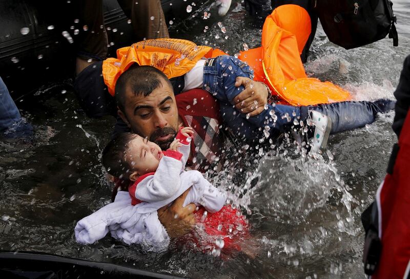 A Syrian refugee holds onto his children as he struggles to walk off a dinghy on the Greek island of Lesbos, after crossing a part of the Aegean Sea from Turkey to Lesbos in September 2015. Photograph: Reuters