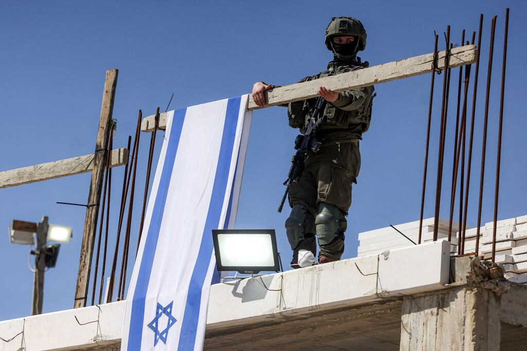 An Israeli army soldier hangs a wooden beam carrying an Israeli flag banner in Hebron city near the Israeli settlement area of Tel Rumeida in the occupied West Bank. Photograph: Hazem Bader/AFP