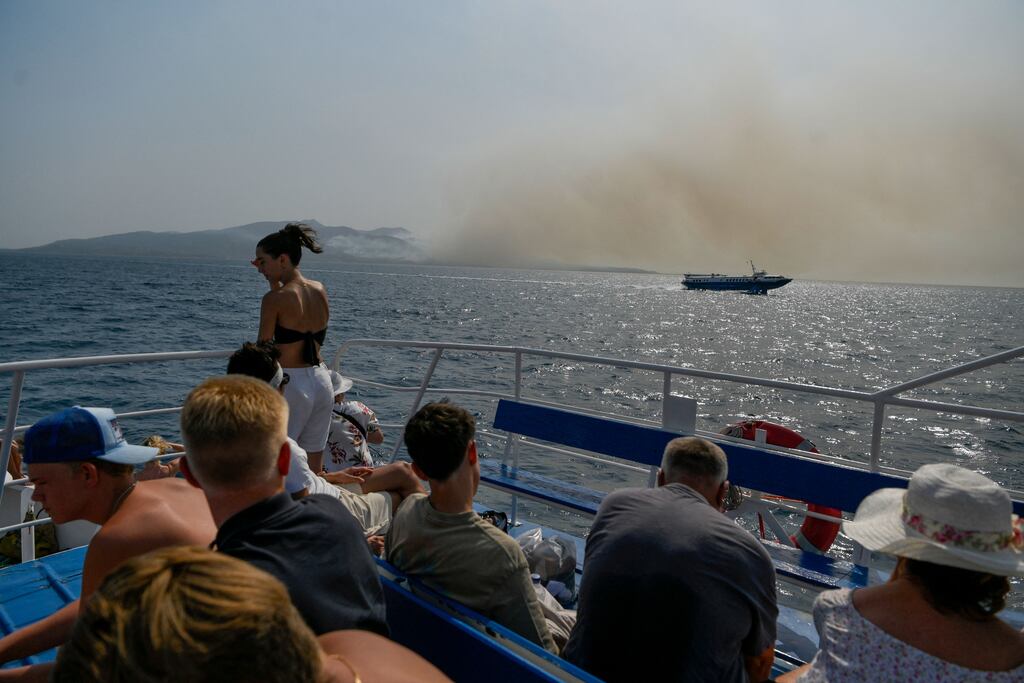 Tourists ride on a ferry to Corfu island as the smoke billows from the fire over the island, on July 25, 2023. Photograph: Getty Images