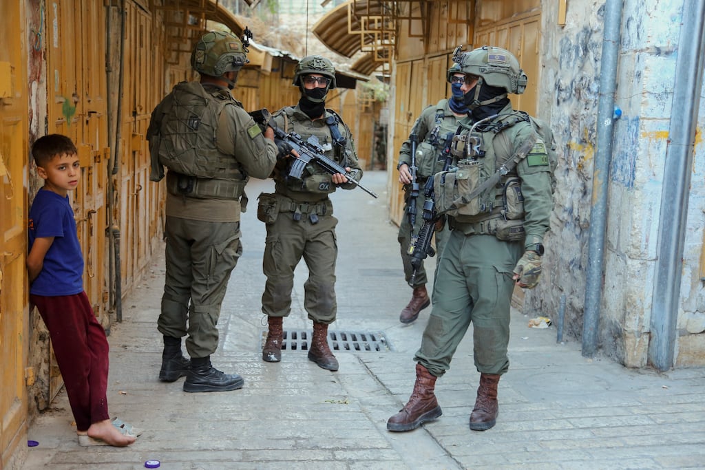 A Palestinian child stands in front of his home as three armed Israeli soldiers guard the area during the settlers' storming of the Old City of Hebron on September 13th, 2025. Photograph: Mosab Shawer/ Middle East Images/ AFP via Getty Images