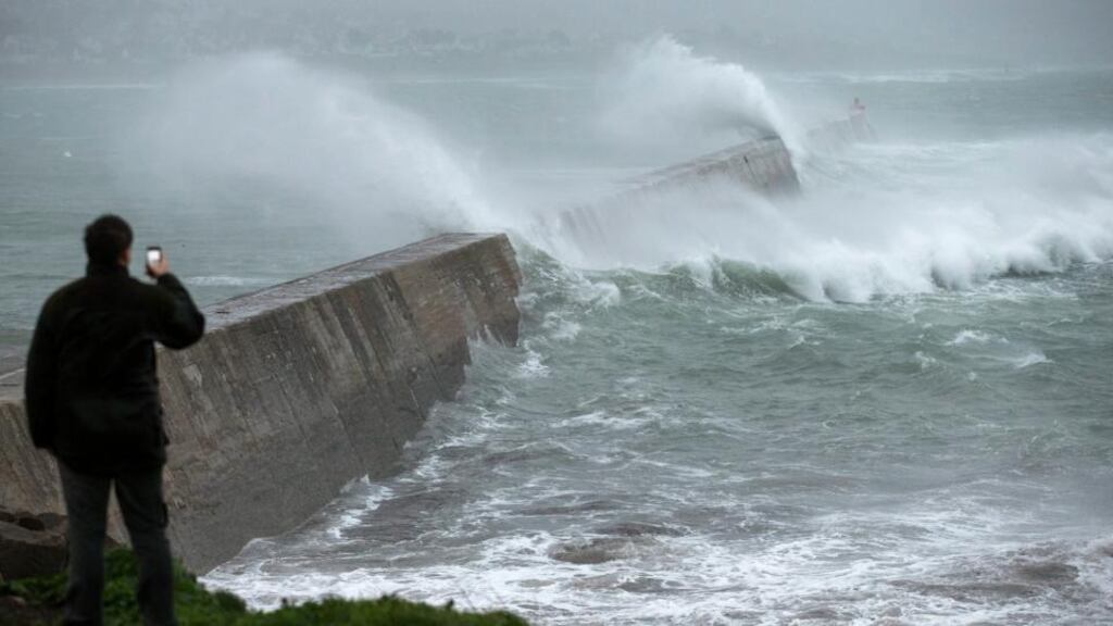 A man looks on as big waves crash against a break-water pier during a storm in Esquibien in Brittany region of France. Photograph: Ian Langsdon/EPA.