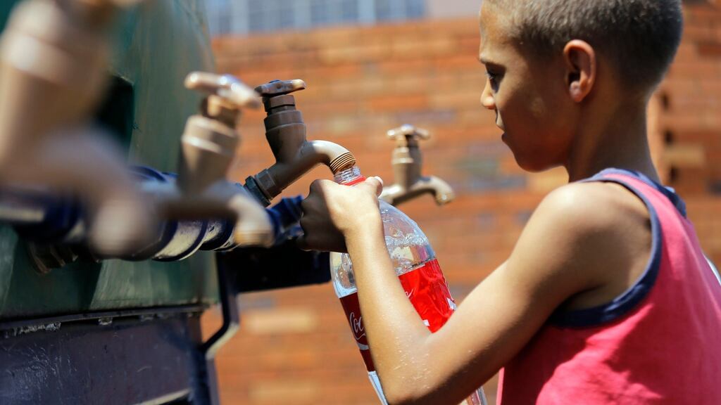 A young boy fills his cup from a water tanker in Coronation, Johannesburg, as South Africa experiences its worst drought in decades. EPA/KIM LUDBROOK