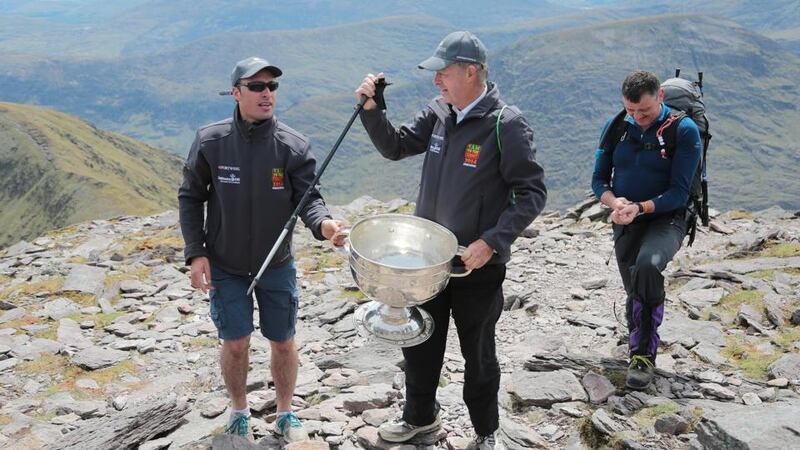 GAA Commentator Mícheál Ó Muircheartaigh lifts the Sam Maguire Cup on the summit of Carrauntoohil with programme director and former Galway star Alan Kerins (left) and Tom Prendergast, 1969 Kerry All-Ireland winner, during the 'Sam to Summit' in aid of the Alan Kerins Project. Photograph: Valerie O’Sullivan/Sportsfile.