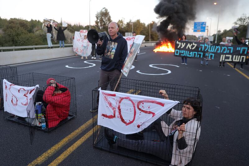 Families and supporters of Israeli hostages held by Hamas in Gaza sit inside cages as they block the main road leading from Tel Aviv to Jerusalem. Photograph: Abir Sultan/EPA