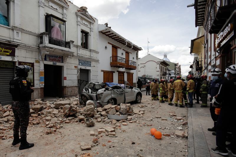 Rescue workers stand next to a car crushed by debris after an earthquake in Cuenca, Ecuador. Photograph: Xavier Caivinagua/AP/PA