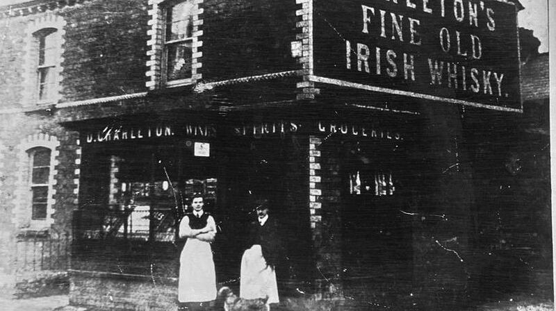 Daniel Charleton standing with his dog and barman outside his pub and shop in Belfast c.1920