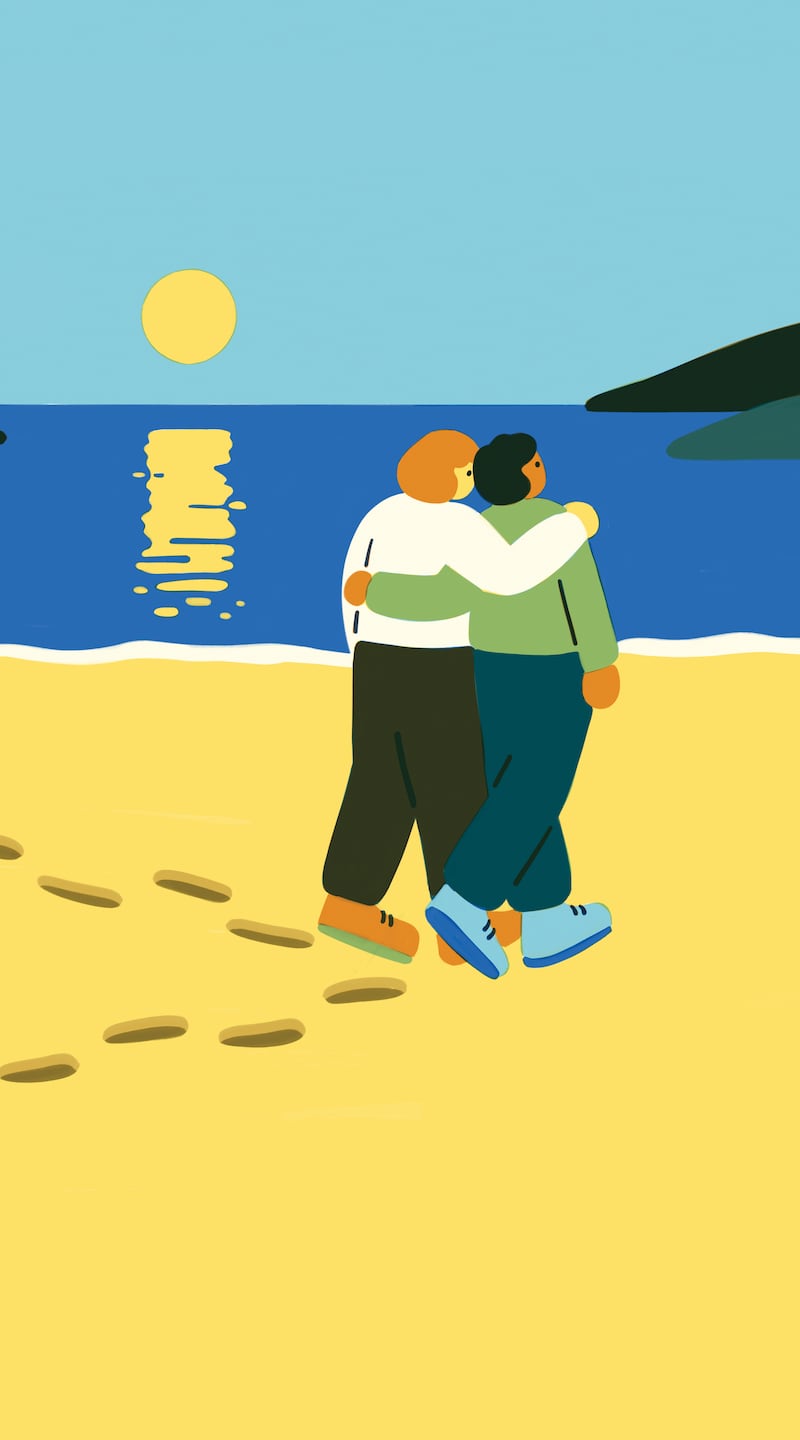 Couple walking arm in arm on a beach at sunset