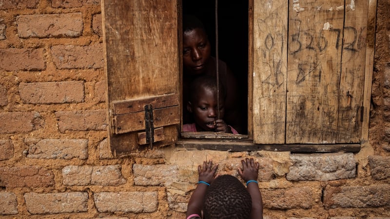 Nono and her daughter Salma peer outside their home as a neighbour’s child looks in. Photograph: Christopher Hopkins