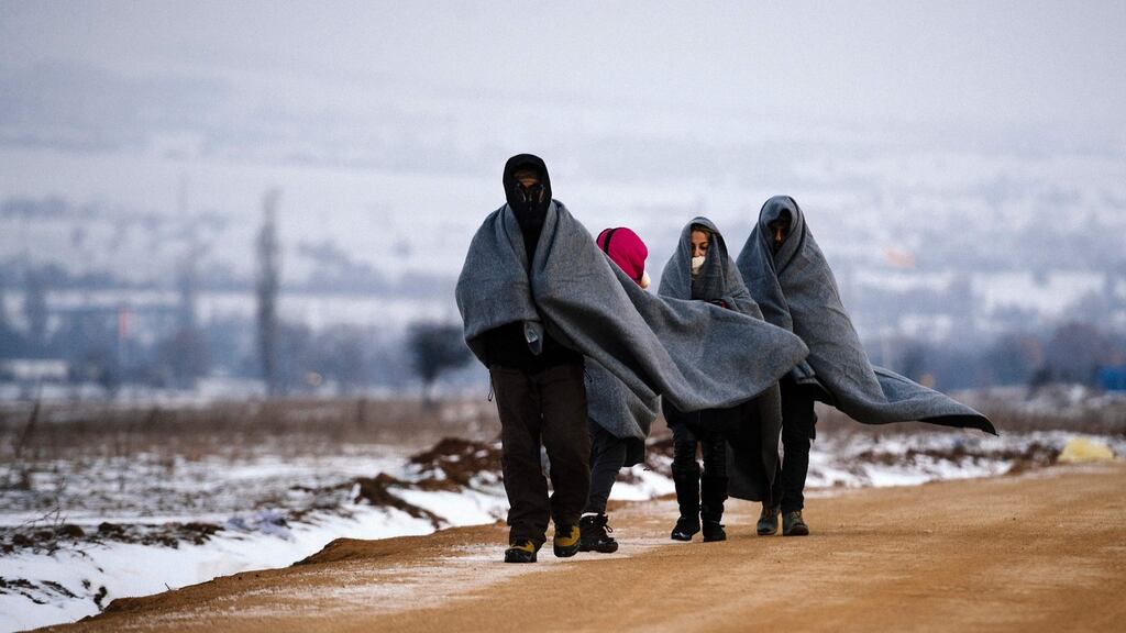 Refugees use their sleeping blankets to keep warm as they walk along snow-covered fields near the Macedonian-Serbian border. Photograph: Dimitar Dilkoff/AFP/Getty Images
