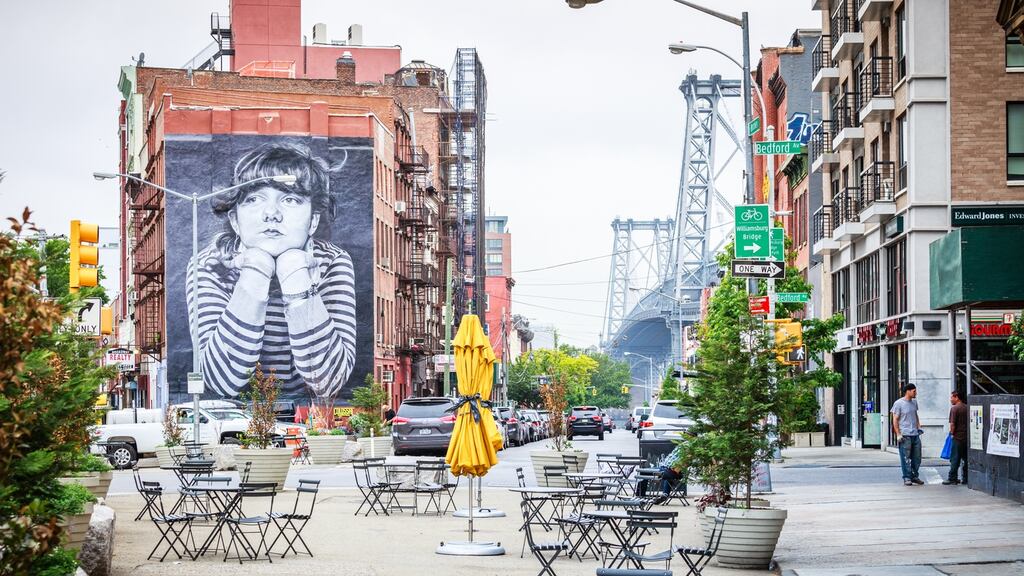 Streetscape in Williamsburg along Broadway with empty chairs on hazy day. Williamsburg bridge is visible in the background.