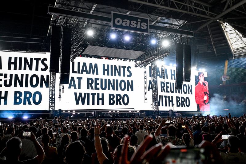 Oasis: Giant screens show press coverage teasing of the band's possible reunion at the back of the stage on the opening night of their Live ’25 Tour at Principality Stadium in Cardiff. Photograph: Gareth Cattermole/Getty Images
