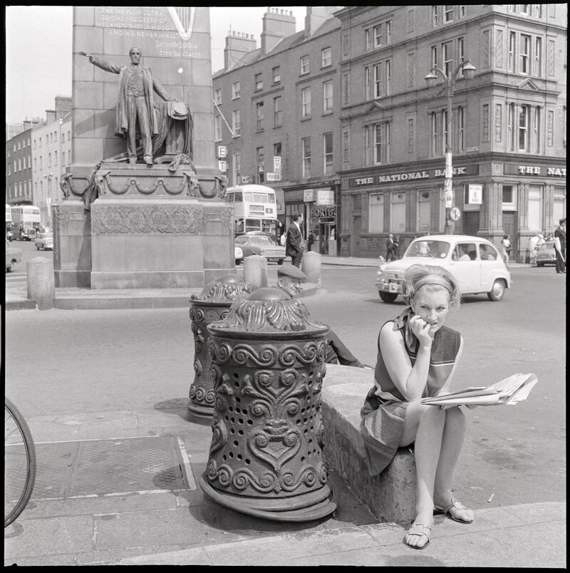 Bollards – Woman sitting beside ornate ironwork bollard on O’Connell Street, Dublin, June or July 1969
