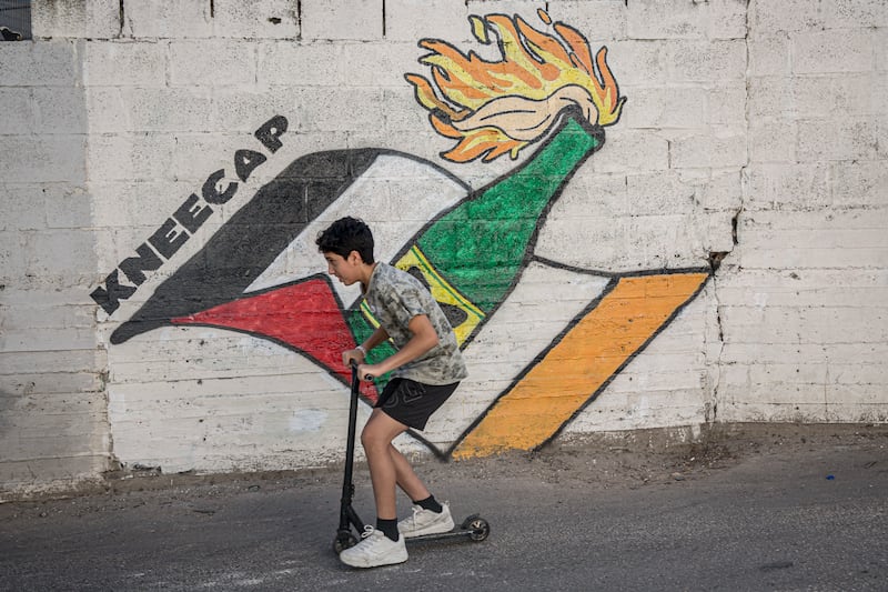A boy on a scooter passes a mural honouring Kneecap in Aida refugee camp