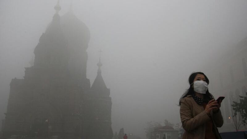 A woman wearing a mask checks her mobile phone during a smoggy day on the square in front of Harbin’s landmark church, in China’s Heilongjiang province. Photograph: Reuters