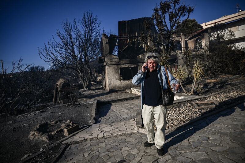A man talks on his phone as he stands next to a burnt house following a wildfire in Thymari, southeast of Athens. Photograph: ARIS MESSINIS/AFP via Getty Images